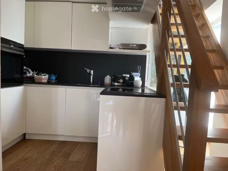 Modern kitchen with white cabinets, black countertops, and stainless steel appliances. Features an oven, stove, and a faucet, with a staircase visible in the background.