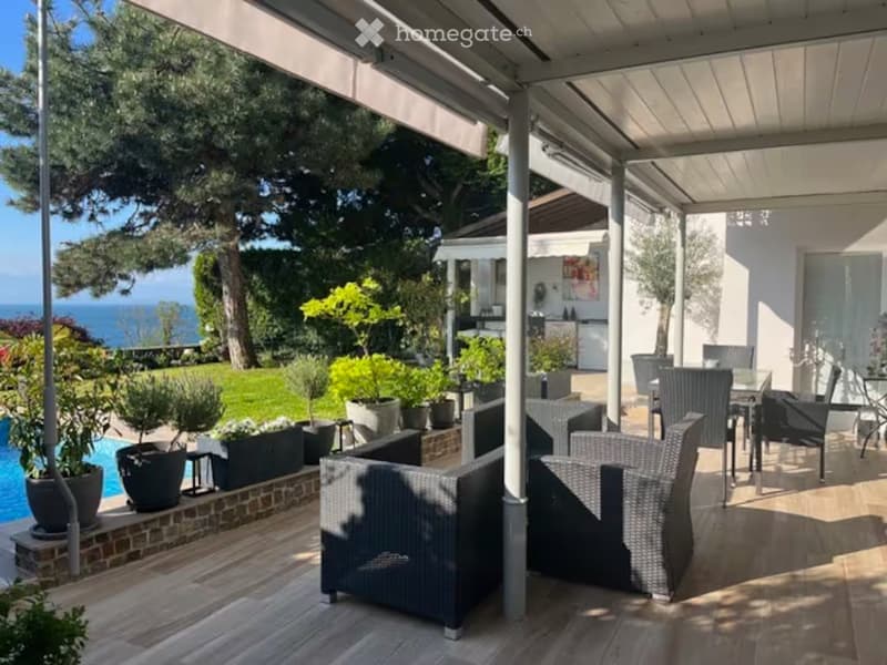 A spacious outdoor patio with wicker furniture, a swimming pool, potted plants, and a scenic ocean view in the background.