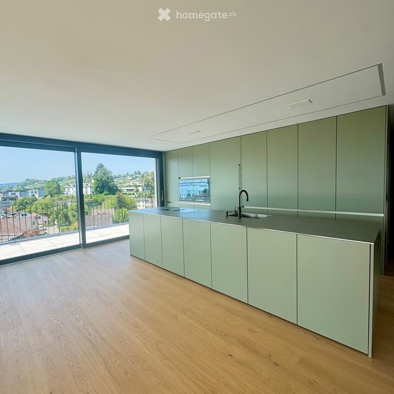 Modern kitchen with light green cabinets, a sleek countertop, and a large window offering a scenic view of the surrounding area.