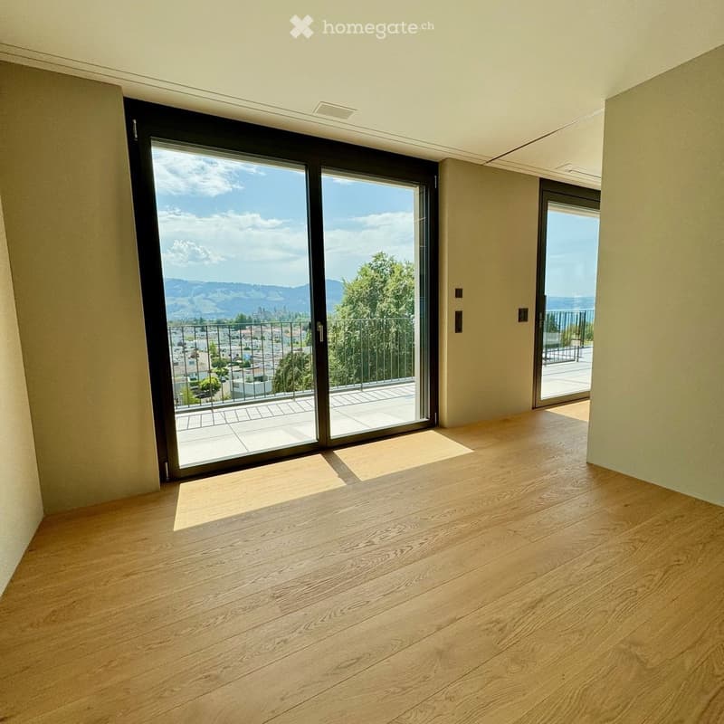 Empty room with wooden flooring, large sliding glass doors leading to a balcony with scenic mountain views.