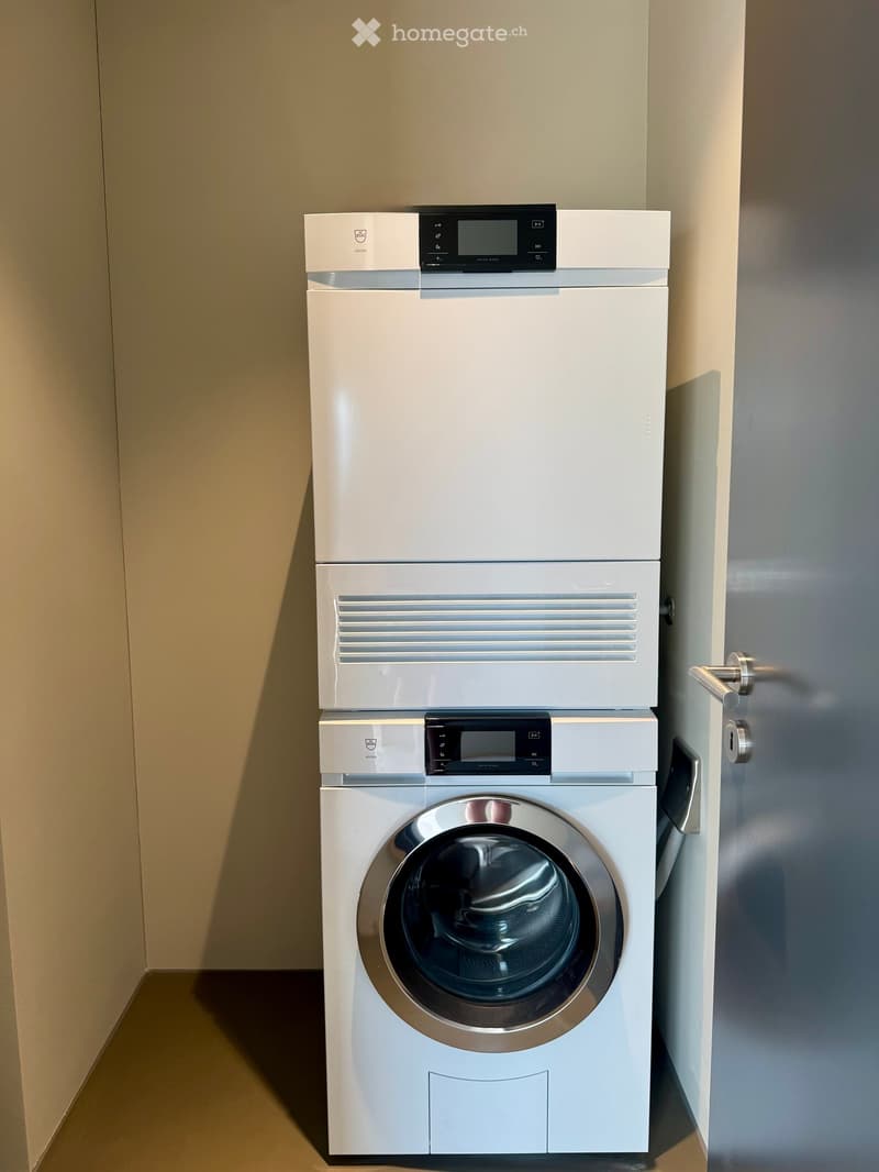 A modern bathroom features a stacked washing machine and dryer unit with sleek white finishes and digital control panels.
