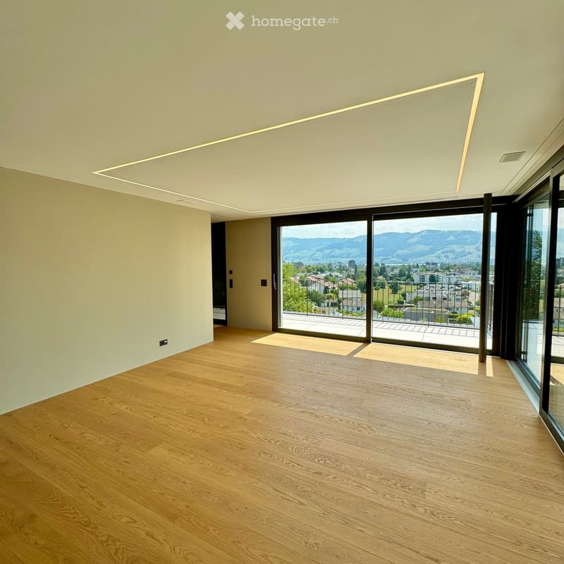 Empty room with wooden flooring, large windows, and a view of the city and mountains.