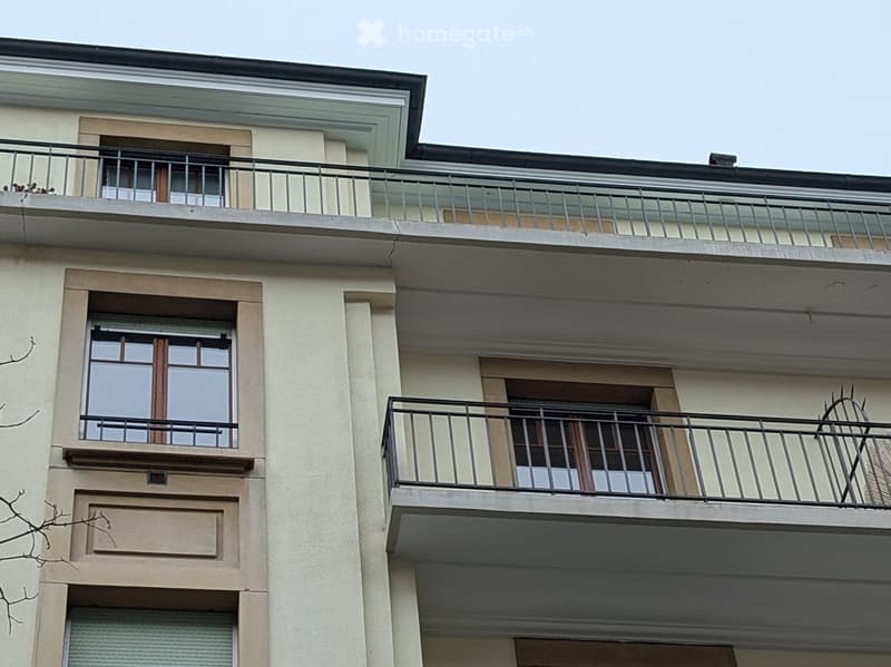 Multi-story residential building with balconies, large windows, and metal railings.