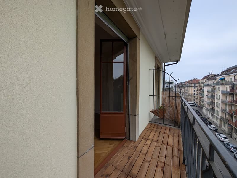 Balcony with wooden decking, metal railing, and a view of the city street and surrounding buildings.
