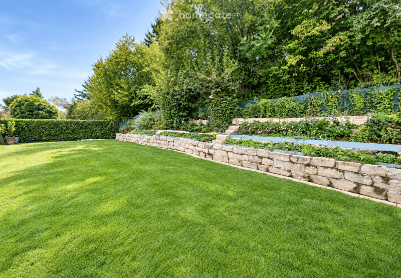 Well-maintained garden with a neatly trimmed lawn, stone retaining wall, and various plants and trees.