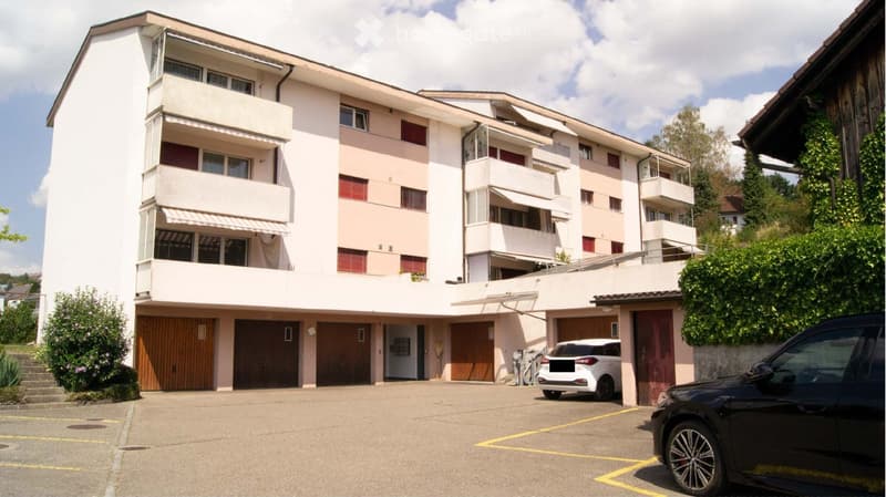 Modern multi-story residential building with balconies, garage, and parking area.