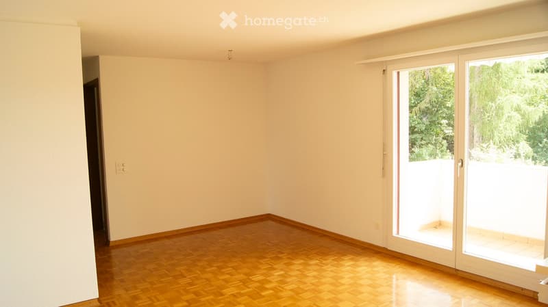 Empty room with wooden flooring, white walls, and large sliding glass doors leading to a balcony or outdoor area.