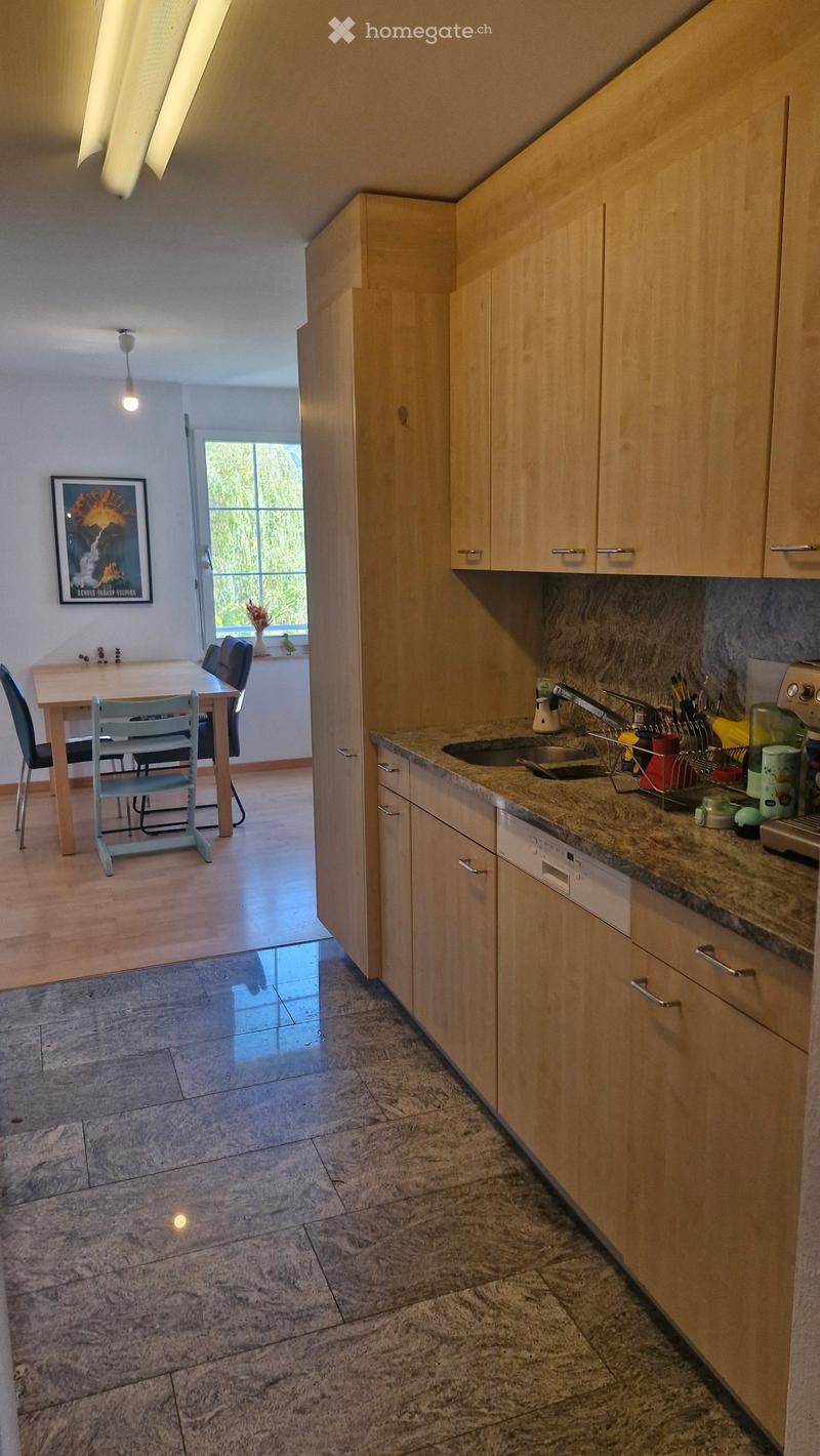 Modern kitchen with light wooden cabinets, granite countertops, and a sink. Adjacent dining area with a table and chairs, large window with a view, and a framed picture on the wall.