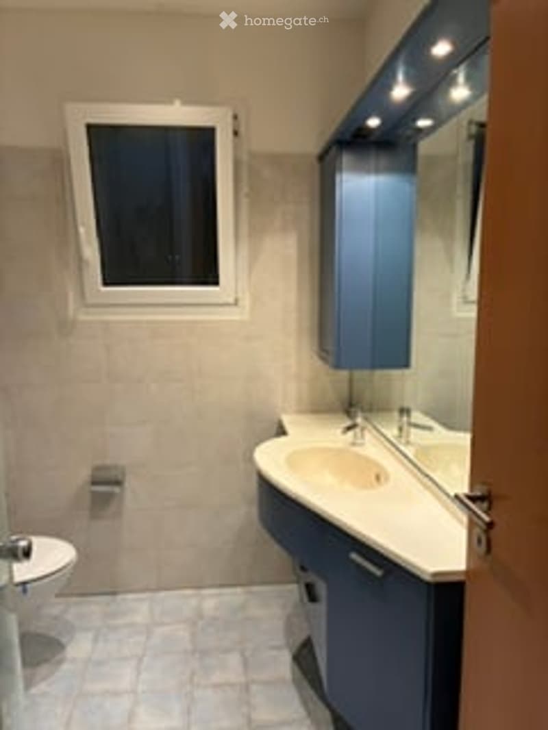 Modern bathroom with a white tiled floor, a blue cabinet, a sink with a mirror, and a toilet.