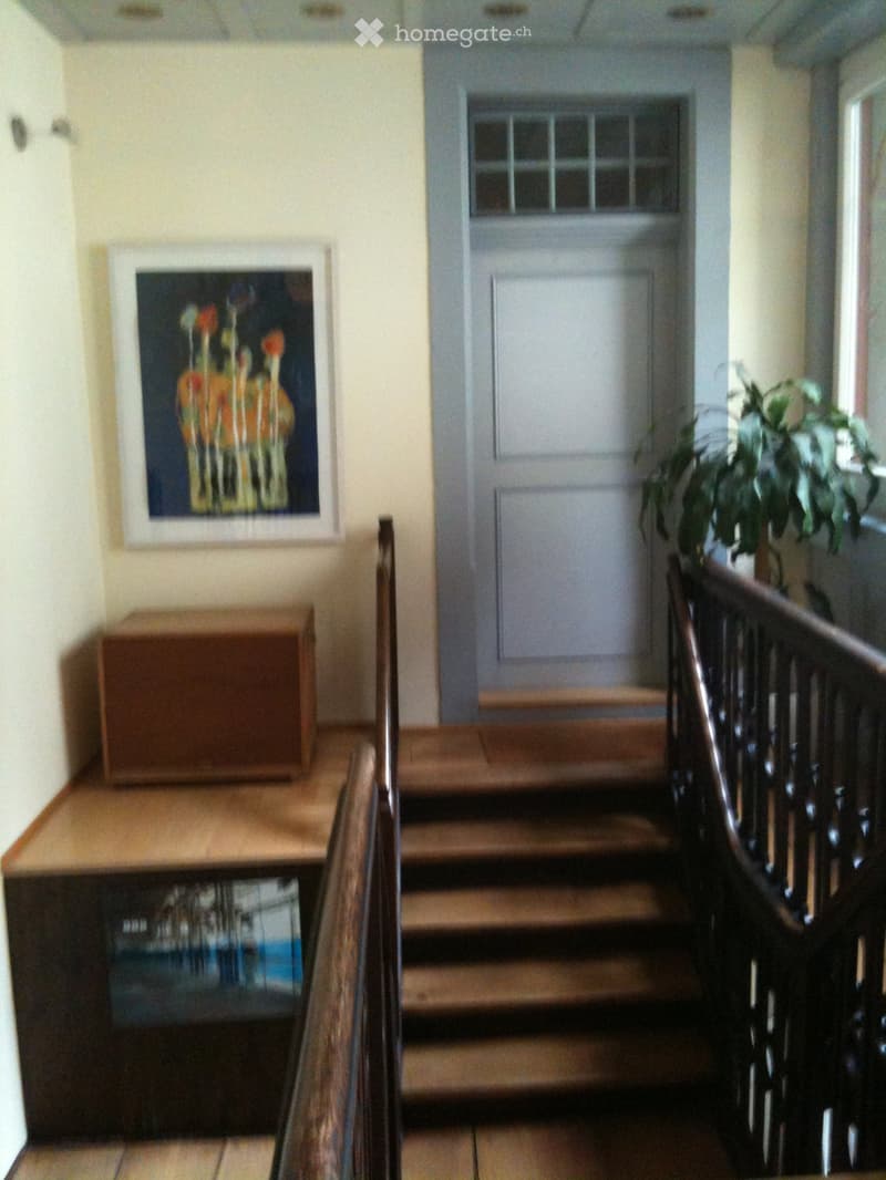 Hallway with wooden staircase, railing, small table, and framed artwork on the wall.
