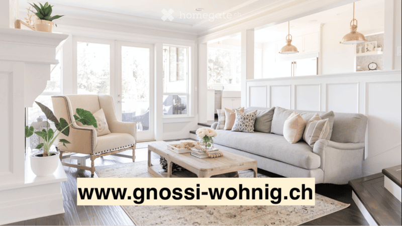 Bright living room with large windows, grey sectional sofa, wooden coffee table, armchair, and decorative plants.