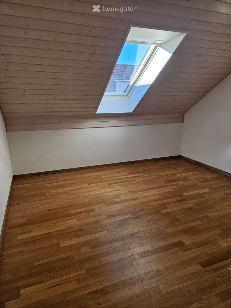 Empty room with wooden flooring and white walls, featuring a skylight window in the ceiling.
