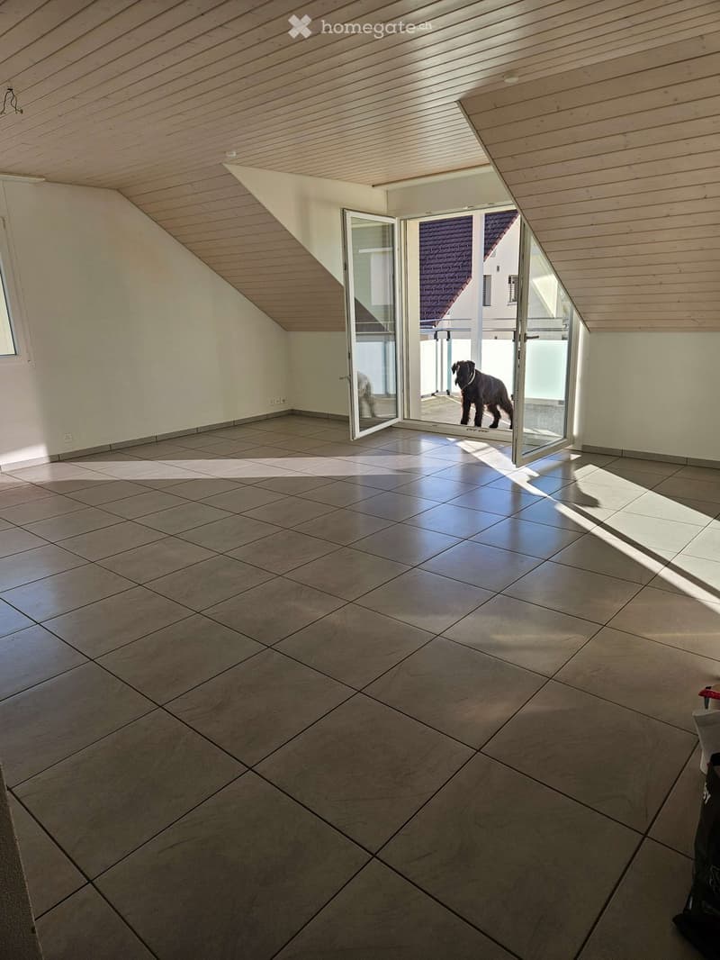 Empty room with tiled floor and wooden slatted ceiling, featuring large glass doors leading to an outdoor area.
