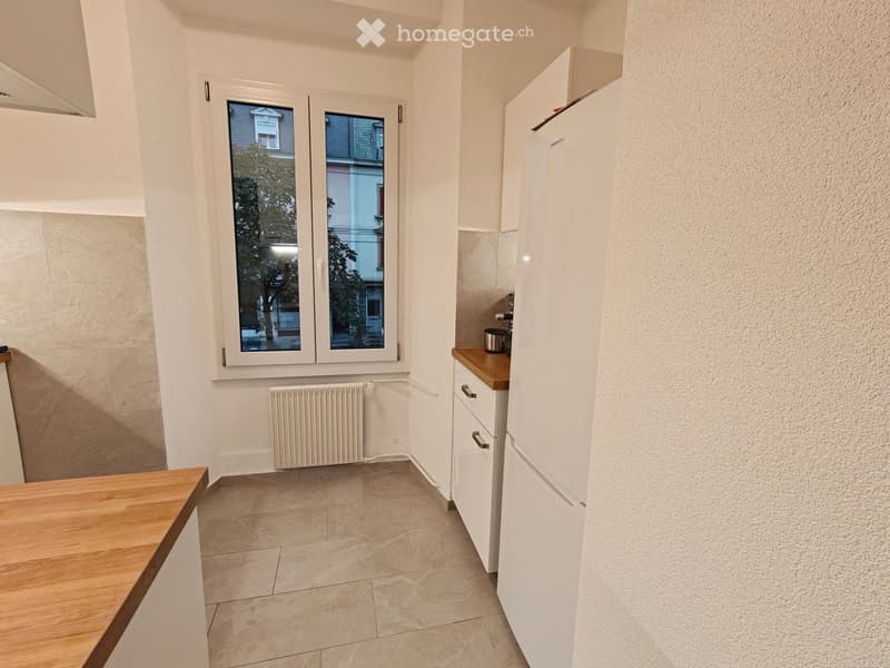 Modern kitchen with white cabinets, a refrigerator, wooden countertops, tiled floor, and a window overlooking a street.