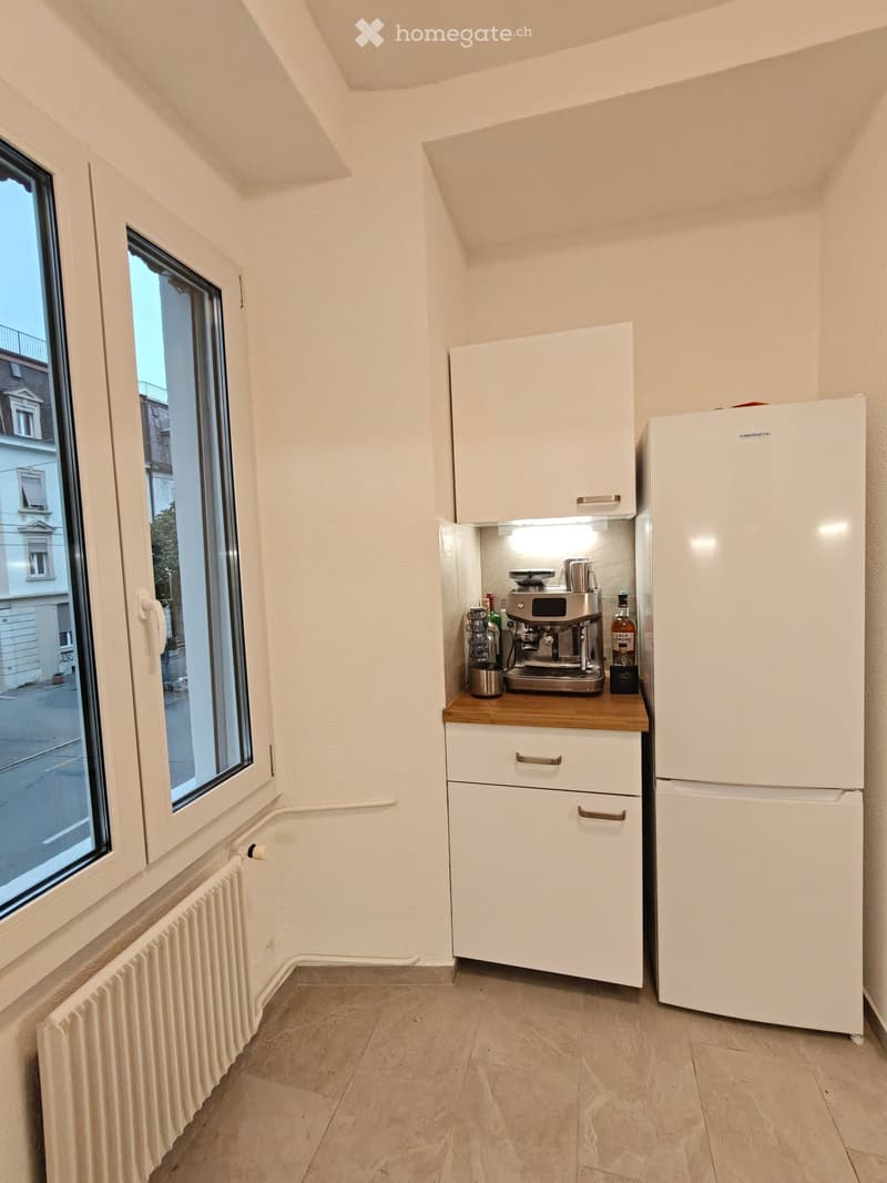 Compact kitchen with white cabinets, a refrigerator, and a coffee machine on a wooden countertop.