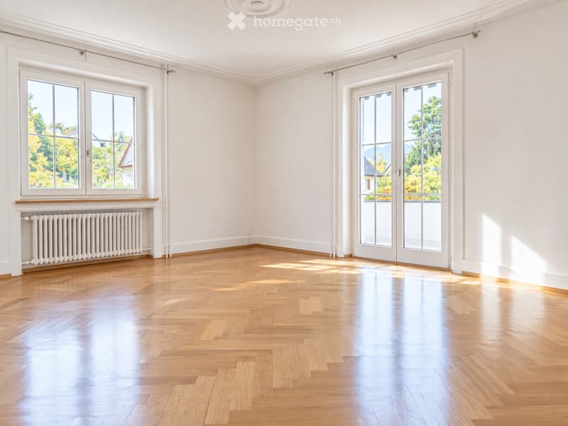 Empty room with light wooden flooring, white walls, large windows, and a radiator. No furniture or equipment present.