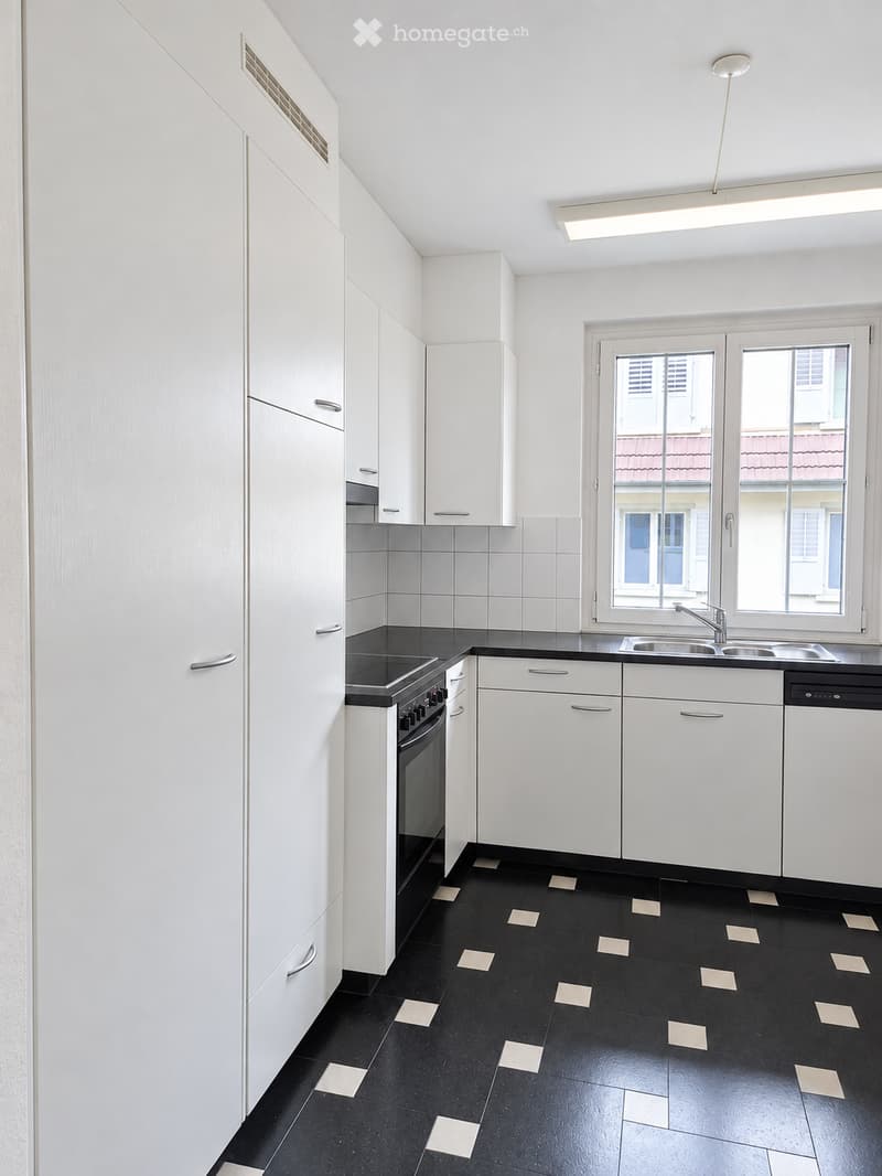 Modern kitchen with white cabinets, black countertops, and black tiled floor with light square accents. Features a sink, faucet, oven, and dishwasher.