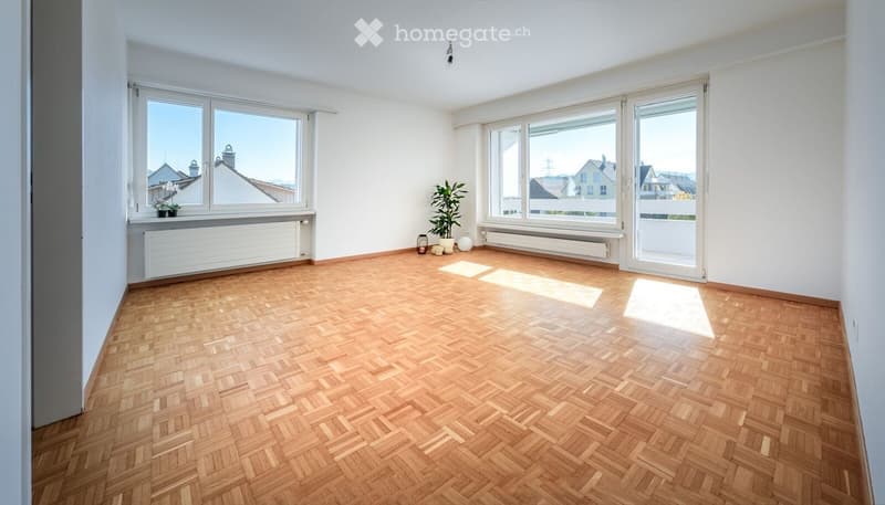 Empty room with wooden herringbone flooring, large windows, radiators, and a small plant in the corner.