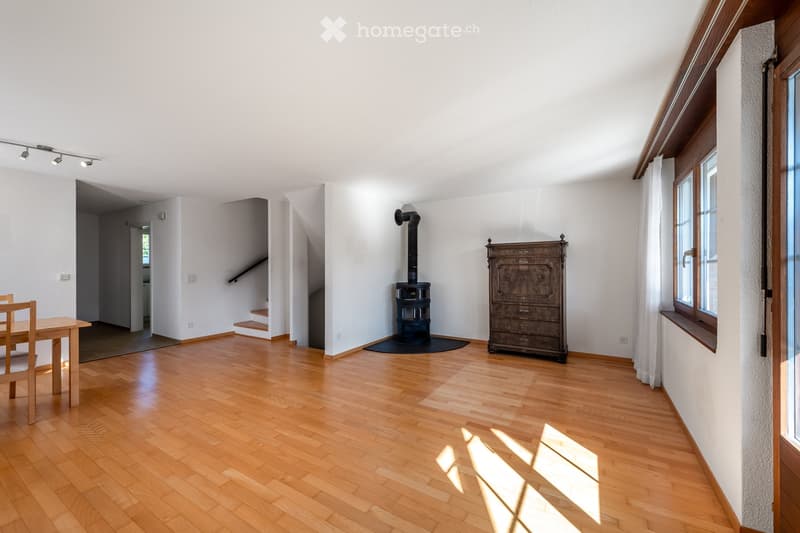 Bright living space with wooden flooring, a wood-burning stove, a wooden cabinet, and a small dining area with a table and chair.
