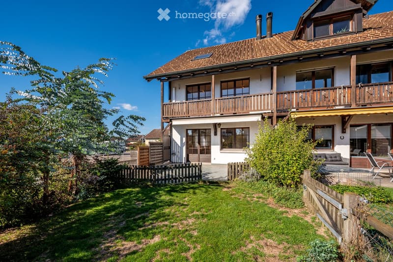Two-story house with a tiled roof, wooden balcony, and well-maintained garden with a lawn and wooden fence.