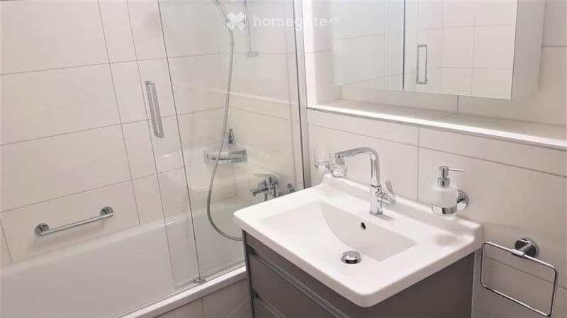 Modern bathroom with white tiles, a sink with a chrome faucet, a mirror cabinet, and a shower area with a glass enclosure.