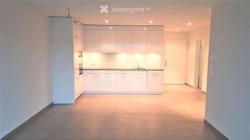 Modern, minimalist kitchen with white cabinets, a central island, and a sink. The space is well-lit with recessed lighting and has a clean, uncluttered design.