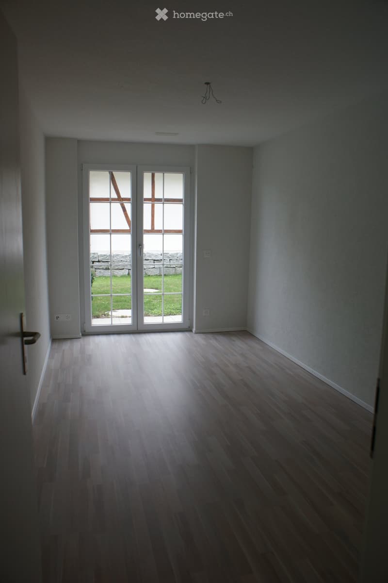 Empty room with wooden flooring, white walls, and a large sliding glass door leading to a grassy outdoor area.