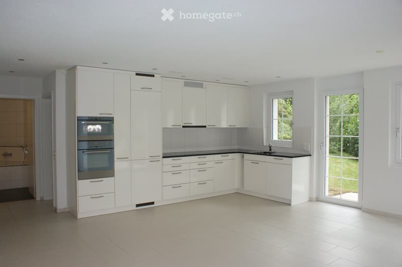 Modern, unfurnished kitchen with white cabinets, stainless steel oven, and a black countertop.