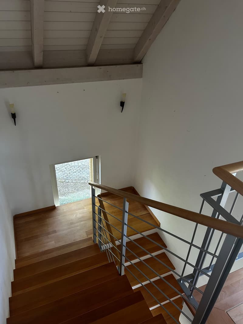 Wooden staircase with metal railing, white walls, and modern lighting fixtures.