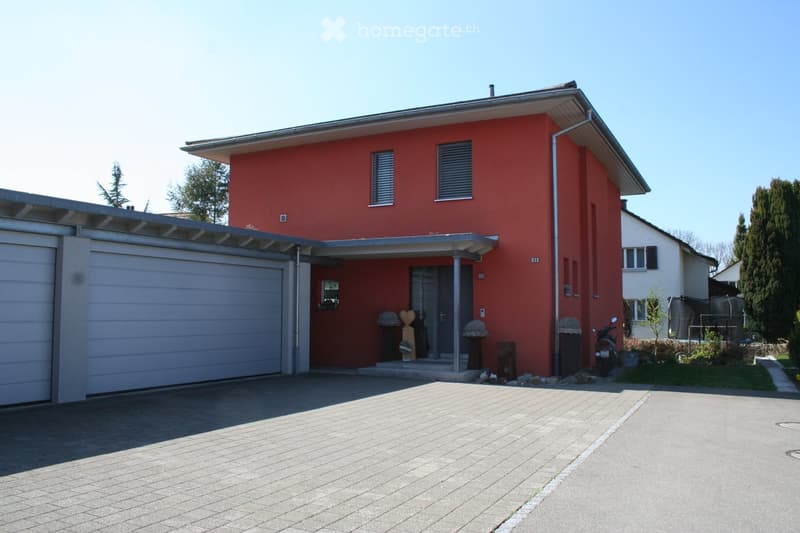 Two-story red house with a modern design, featuring a garage, covered entrance, and a paved driveway.