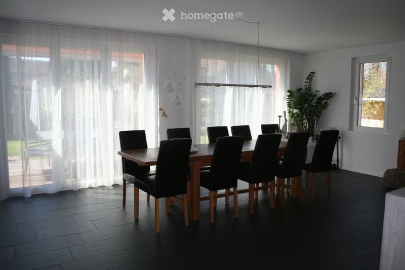 Dining room with a wooden dining table surrounded by black chairs, pendant lights, and a plant in a vase near the window.