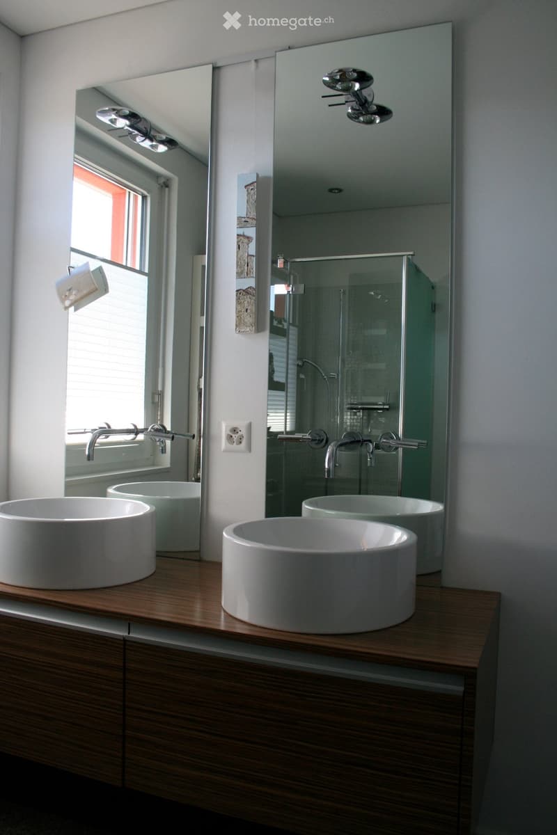 Modern bathroom with two white sinks on a wooden vanity, large mirror, and glass shower enclosure.