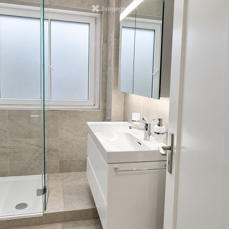 Modern bathroom with a white sink, chrome faucet, mirrored cabinet, and a glass-enclosed shower area.