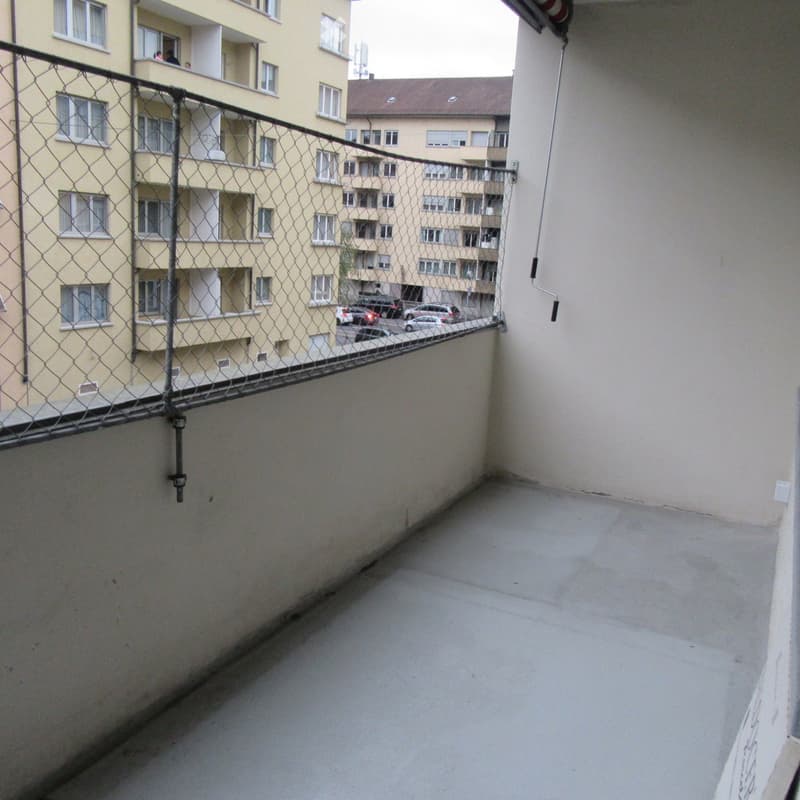 Narrow balcony with metal railing, overlooking a multi-story residential building with several windows and balconies.