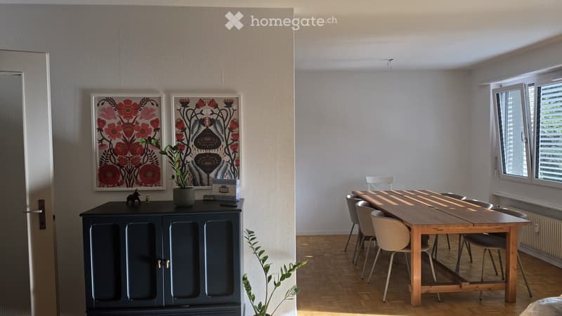 Bright dining area with a wooden table, chairs, a dark blue cabinet, and two framed floral pictures on the wall.