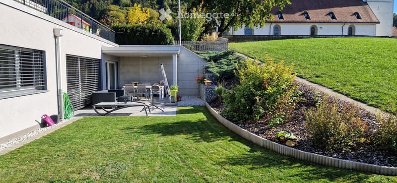 Well-maintained garden with a patio area, outdoor furniture, and a modern house in the background.