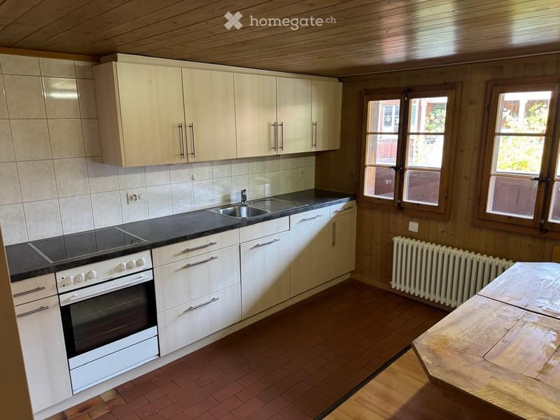 Modern kitchen with white cabinets, stainless steel sink, electric oven, and wooden table.