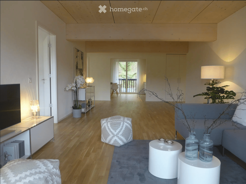 Modern living room with wooden flooring, grey sofa, ottoman, coffee table, side tables, vases, and a balcony access.