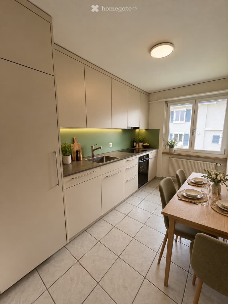 Modern kitchen with light-colored cabinets, a central island, and a dining area. Features include a sink, oven, and a dining table with chairs.