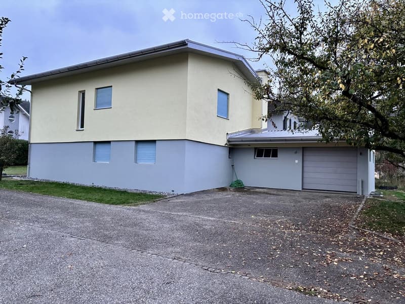 Two-story house with beige and grey exterior, multiple windows, garage, and driveway.