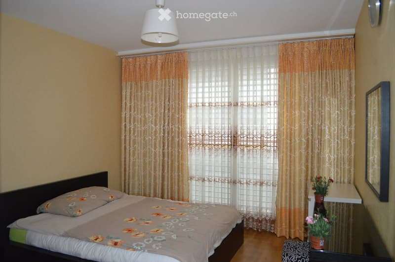 Cozy bedroom with a double bed, nightstand, mirror, and potted plants on a small table.