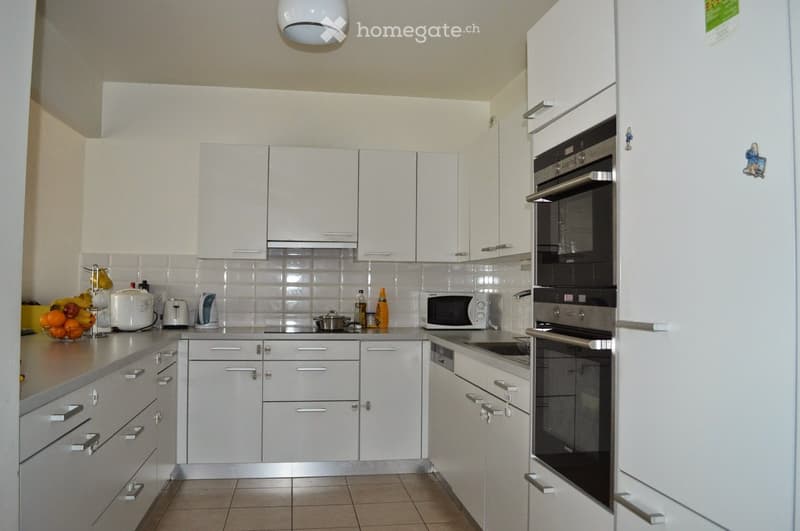 Modern kitchen with white cabinets, stainless steel appliances, and a fruit bowl on the counter.