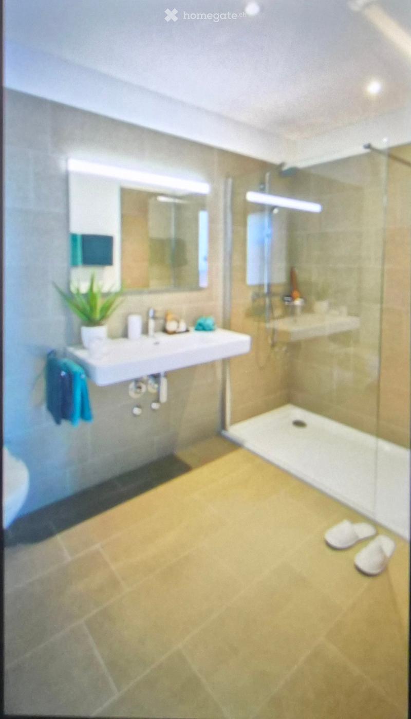 Modern bathroom with a white sink, large mirror, glass-enclosed shower, and beige tiled floor.