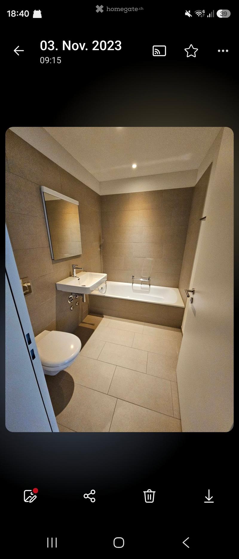 Modern bathroom with beige tiles, a white sink, bathtub, toilet, and a large mirror.