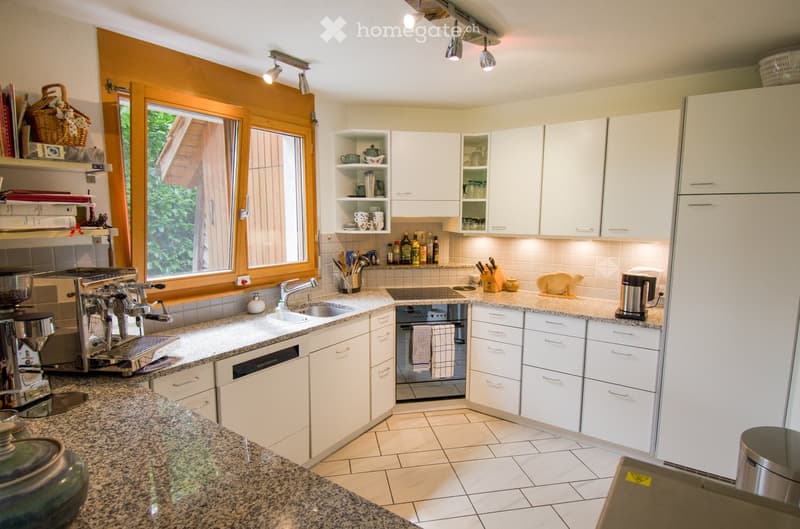 Modern kitchen with white cabinets, granite countertops, stainless steel appliances, and ample natural light from large windows.