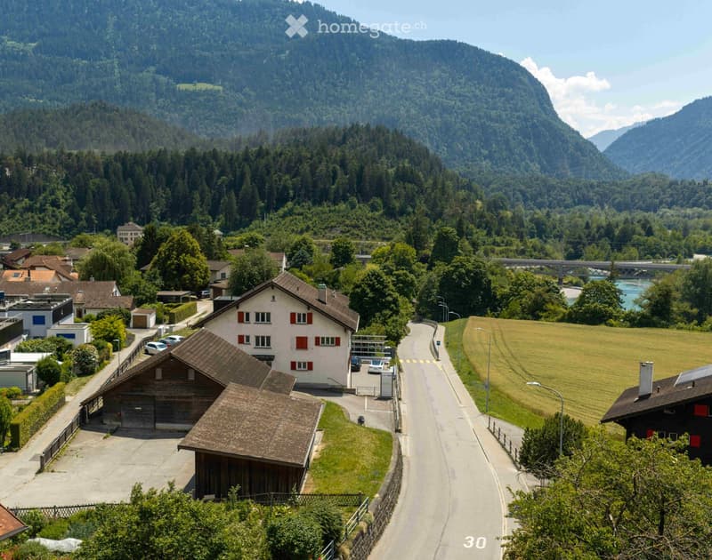 A scenic view of a village nestled in a valley with houses, a road, and surrounding mountains.