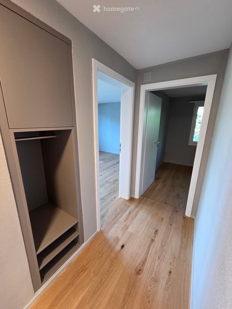 Empty hallway with light wooden flooring, built-in closet on one side, and two open doors leading to other rooms.