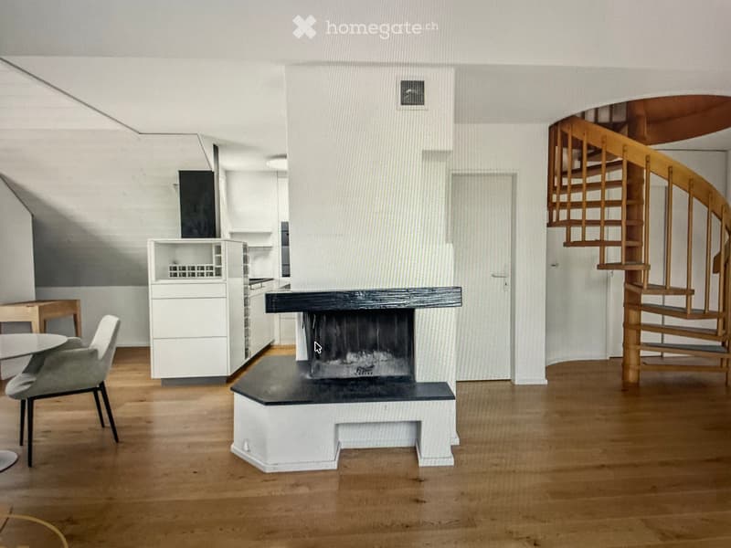 Modern living space with a fireplace, a chair, a small table, and a kitchen area with white cabinets.