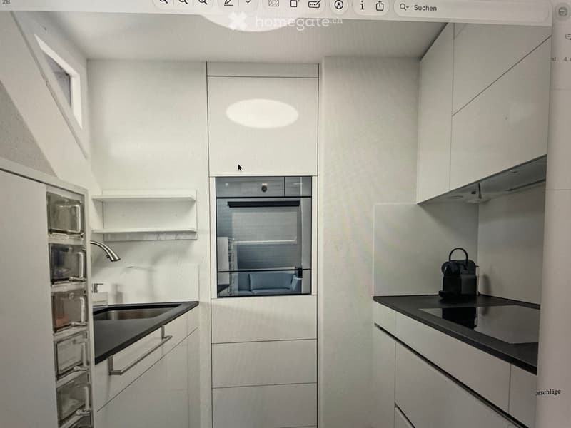 Modern kitchen with white cabinets, black countertops, stainless steel sink, and built-in oven. A coffee maker is placed on the counter.