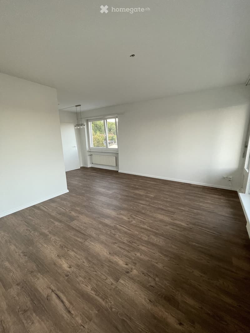 Empty room with wooden flooring, white walls, and a window with a view of greenery. No furniture or equipment is present.